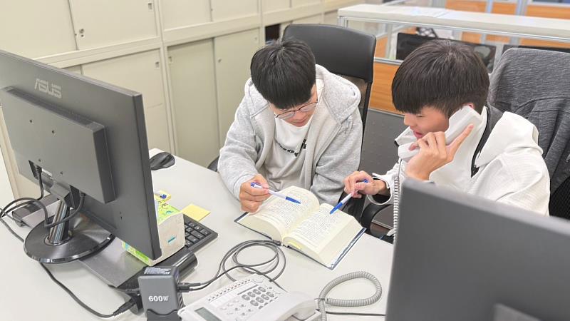 暑期工讀生劉向宏與孫勖宸接聽諮詢電話翻閱書籍討論的照片