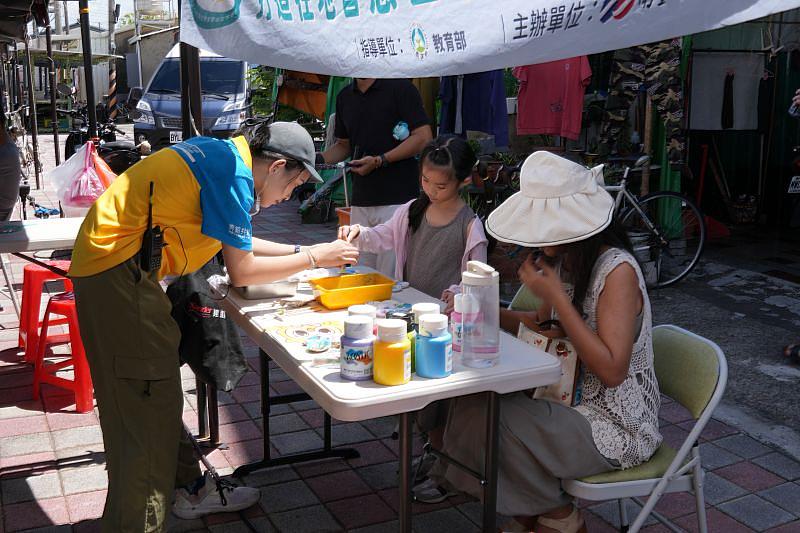 青銀共創USR計畫團隊學生（左1），協助旅客製作蚵殼彩繪與蚵殼風鈴。