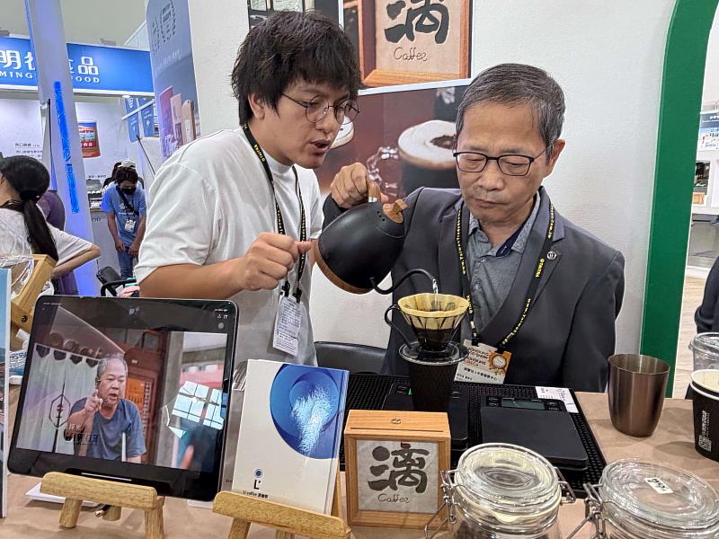 中衛發展中心董事長謝明達(右)在展會中,親自體驗高雄桃源區布農族青年謝瑜璇創立的「漓咖啡」手沖咖啡,謝瑜璇(左)在旁細心解說,展現中衛中心對在地特色產業與青年創業的支持與關注,展後也會協助上架多元通路。