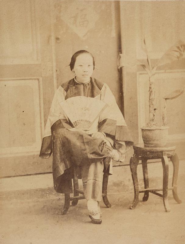 〈婦人〉 日人廣部正三於1896年2月至臺灣遊歷，〈婦人〉為其收集、製作之臺灣影像寫真帖內照片之一。 本照片為在室內攝影的一婦人，旁邊有盆栽。婦人頭髮往後梳，微露齒而笑，眼神自然。穿著大襟衫，右手持扇，左手腕戴著玉環。婦人纏足，但蹺腳拍照，姿態怡然自得。