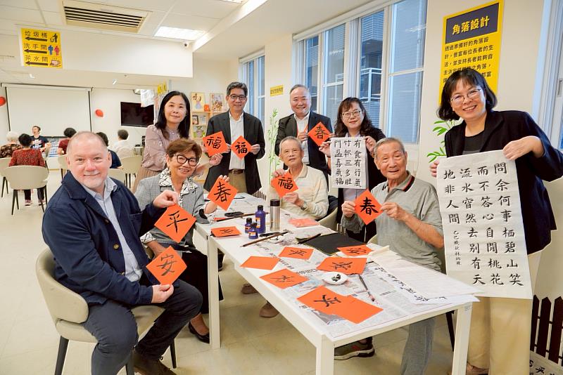 Rick博士（左1）、譚孟春教授（左2）與社會局專門委員林秀穗（右3）等人手拿紅宣紙及書法作品合影留念