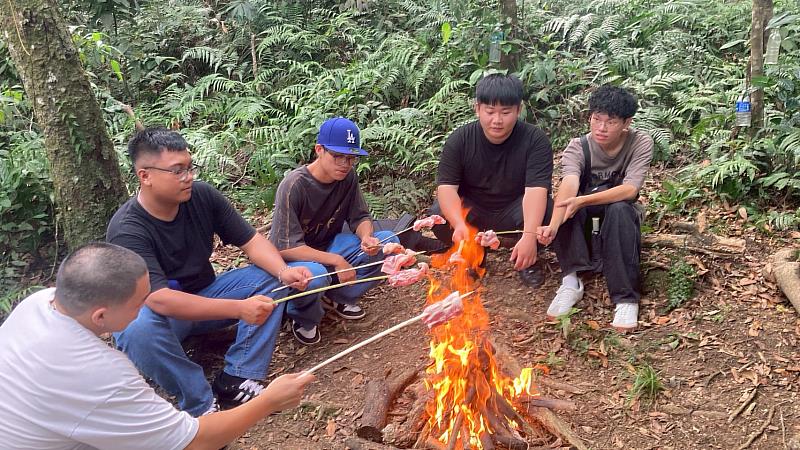 學生們圍坐營火旁烤山豬肉，體驗原住民族狩獵後共享的野宴文化。