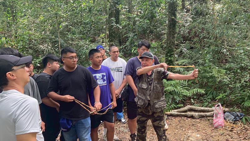 學生們認真聆聽給樹營地校長示範彈弓射擊技巧，學習傳統狩獵技藝。