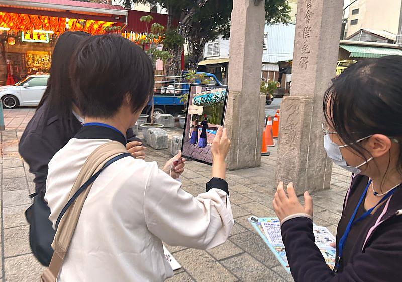 永村景子副教授體驗南臺科大計畫團隊開發的MR(混合實境)遊戲。此遊戲在接官亭歷史文化景點,重現清代官員乘船出現在接官亭前、上岸到風神廟赴任的情景,展現科技在重現文化記憶方面的實戰應用。