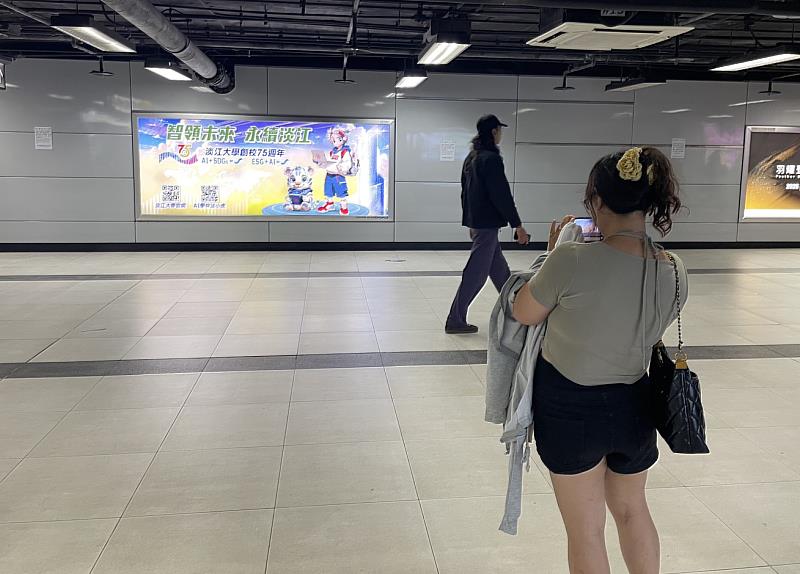 不少路過捷運臺北車站的旅客，一眼即被「AI學伴淡小虎與訓練師」捷運燈箱廣告吸引，特地停下腳步拍照。（圖／淡江大學提供）