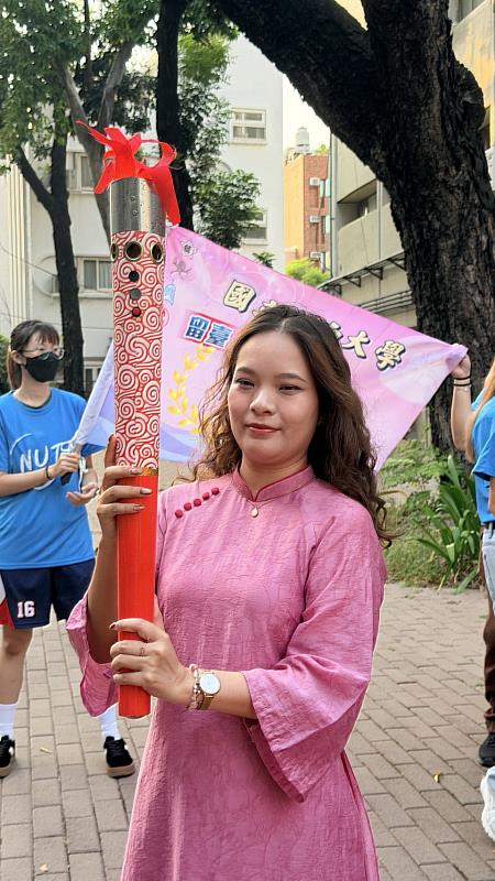 越南籍南大教育系博士班學生身著傳統服飾手持聖火,展現南大國際化與文化多樣性。