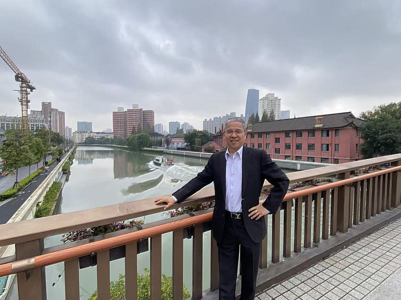 唐彥博校長站在蘇州河畔小橋上，背後可見上海聖約翰大學紅磚校舍遺跡，象徵跨越時空的精神連結。