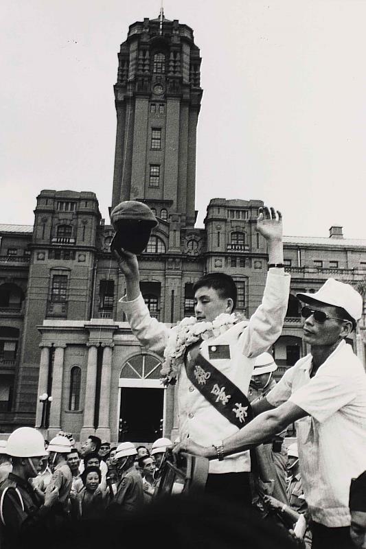 〈小國手魏景林〉 攝影家翁庭華作品,1971年。翁庭華捕抓到總統府高聳建築與小國手魏景林(1958-)的合影,那一瞬間象徵著榮光的片刻、全臺灣人曾經的瘋狂與集體記憶。魏景林為1971年第一代巨人少棒選手,1971年8月29日,臺南巨人少棒隊以3戰3勝的成績,獲得威廉波特世界少棒冠軍。