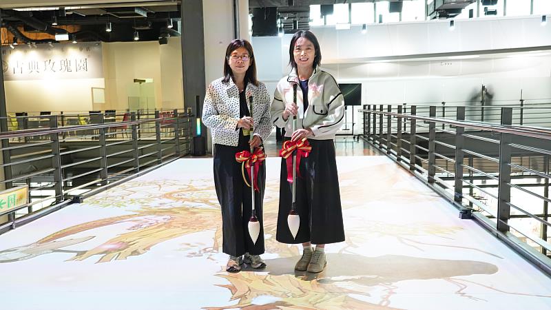 國美館長陳貺怡與郭雪湖基金會顧問謝筱玫以毛筆點墨的方式於空橋上緩緩點出第一筆墨跡，隨即觸發互動投影系統，光影花瓣隨墨韻綻放。