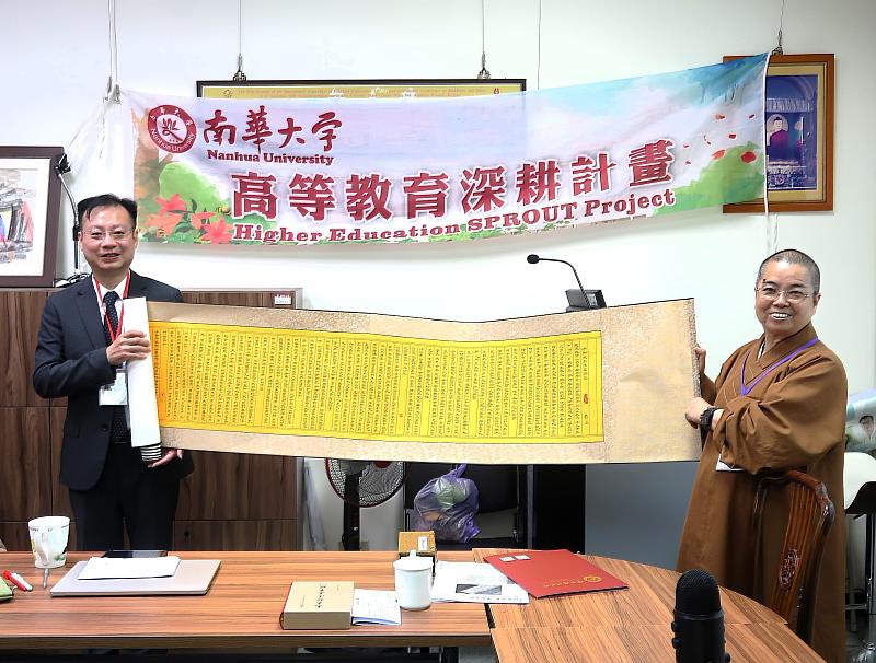 南華大學人間佛教學術講座邀請國立成功大學嚴瑋泓教授(左)詮釋《金剛經》，宗教所所長覺明法師(右)致贈金剛經卷軸。