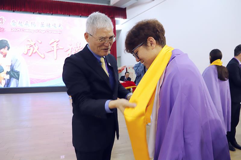 南華大學遵行古禮舉辦成年禮，行「再加禮」，高俊雄校長(左)及師長一一為學子披授黃巾給予祝福。