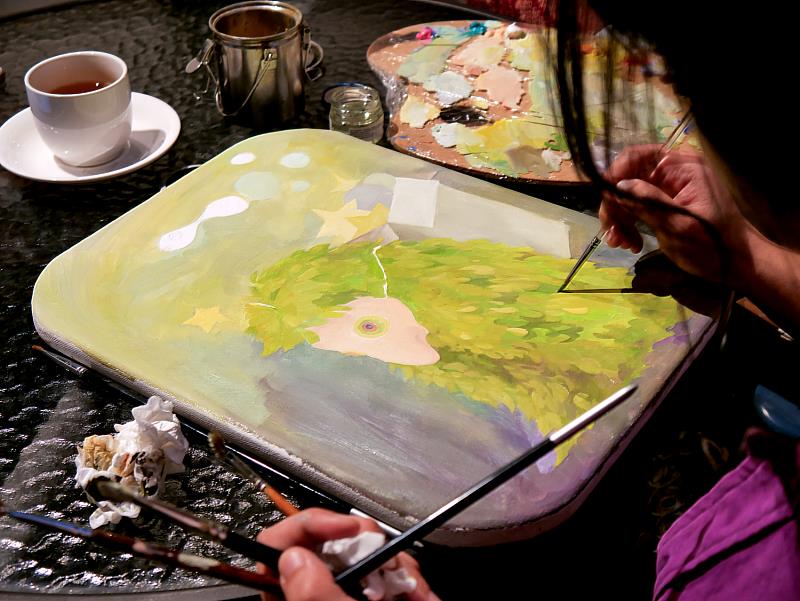 作品細節與調色盤特寫。畫布上的聖誕意象逐漸浮現，搭配一旁調色盤與畫筆，呈現創作「正在發生」的真實瞬間。