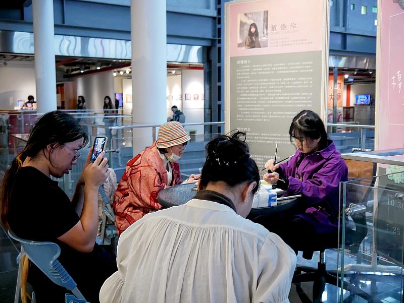 觀眾近距離圍坐欣賞創作過程。活動現場吸引多位觀眾圍坐欣賞，靜靜觀看作品在時間流動中生成，形成溫暖而專注的觀展氛圍。