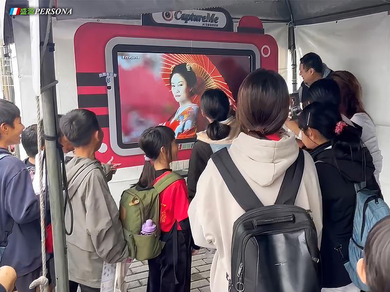 盛源PERSONA攤位上許多親子與師生圍繞在CaptureMe AI互動區域，透過拍照及即時 AI 換臉技術化身不同職業角色，現場充滿歡笑與驚喜，互動氣氛熱烈。