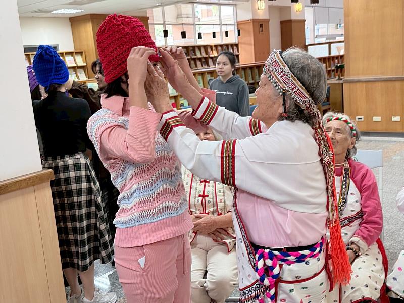 Payi（長者）為編織共學課程學生戴上自己手織的毛帽。