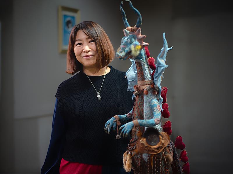 藝術家IWACO與其作品合影，以古布、絲線等看似無序的材質層層縫合，讓柔軟在結構中長出力量；本次將隨鶯歌光點藝術中心參與ONE ART Taipei 2026。