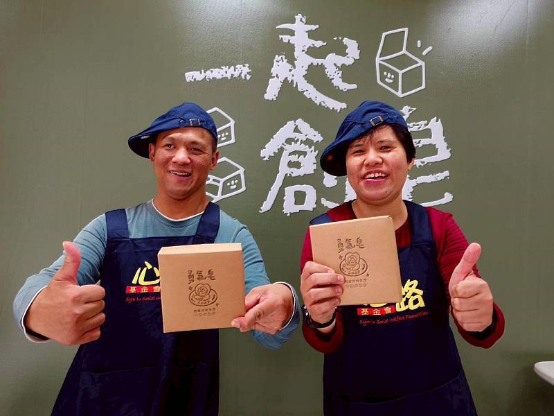 心路工坊青年奕宏與珮珮手拿參與包裝作業的「勇氣皂組」合影，展露自信笑容。圖 / 心路基金會