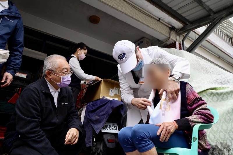 花蓮慈院林欣榮院長（白袍白帽）與特殊需求者牙科主任李彞邦（左1）為阿嬤送上背心新衣與圍巾，祝福溫暖過新年。