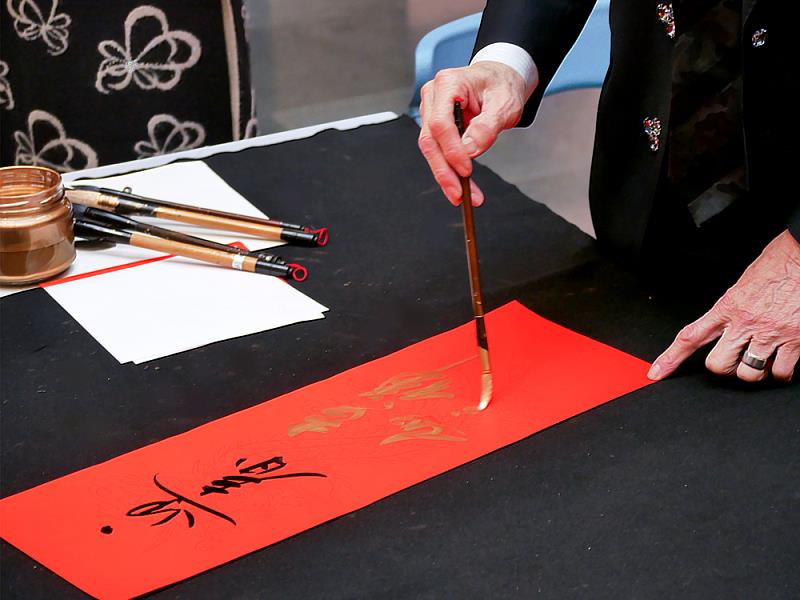 揮毫過程中，老師運筆穩健而從容，墨色與金彩交織於紅紙之上，細節之中展現書法名家的深厚底蘊。