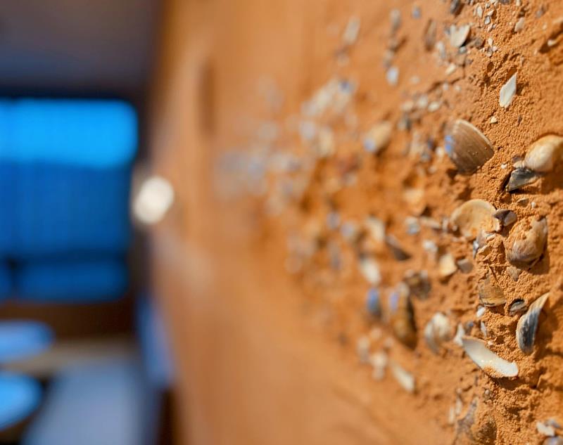 牆面選用苗栗黃土與桃園紅土混入文蛤殼與陶片，手工鏝抹出文化層肌理。