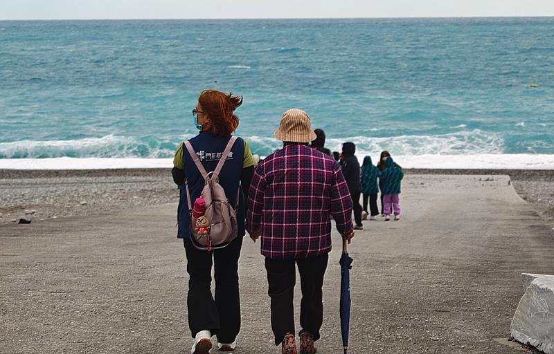 門諾基金會同仁牽著老幼共學的李黃阿嬤走到海岸。