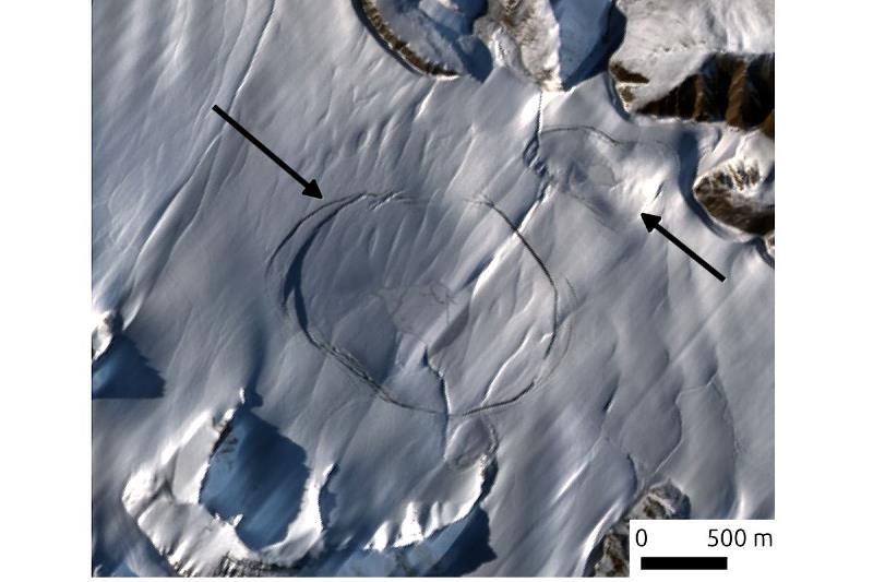 本研究在加拿大艾厄士米爾島北方偵測到的冰下湖的哨兵2號（Sentinel-2）衛星影像。除了周圍山峰外，地表幾乎全被冰覆蓋，但箭頭指向的冰河裂隙勾勒出來的區域，實際上是冰下湖在排水後造成冰河表面凹陷的外緣。／影像來源為歐洲太空總署，由鄭懷傑助理教授後製提供