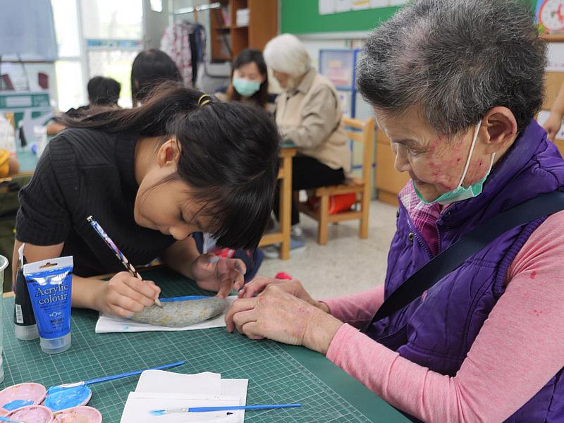 二年級鄰座的邱同學（左）主動協助郭阿嬤（右）描繪飛魚輪廓。