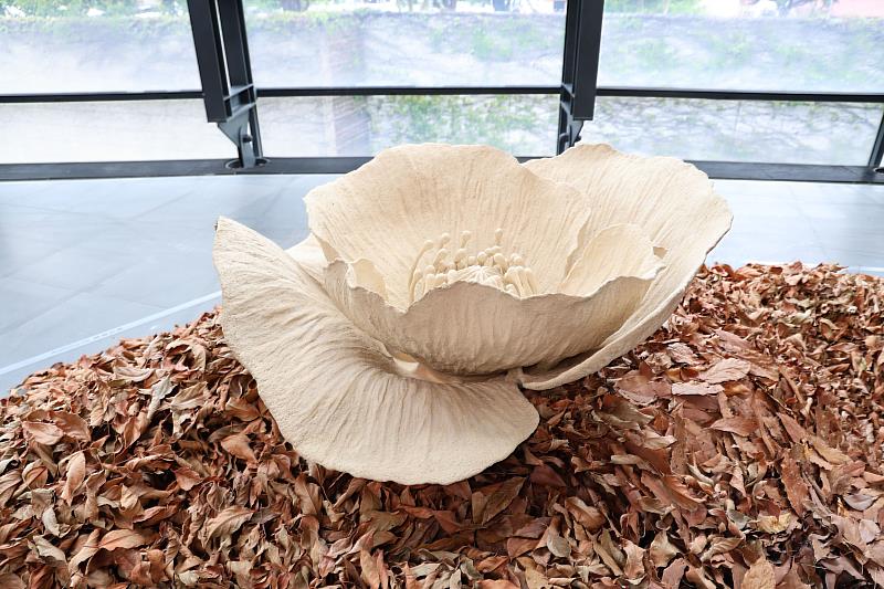 《Flora》以陶土捏塑出巨大罌粟花，並佇立於落葉中，在盛放與枯萎之間映照豐饒與消逝並存。