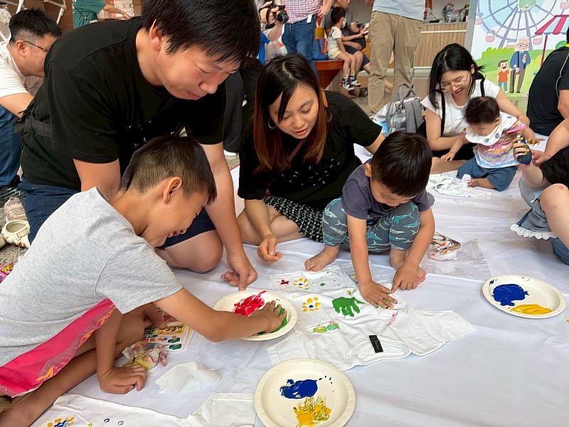 親子衣服彩繪活動中，一家人緊密互動，共同在T恤上蓋印手印，享受溫馨的共同創作時光。