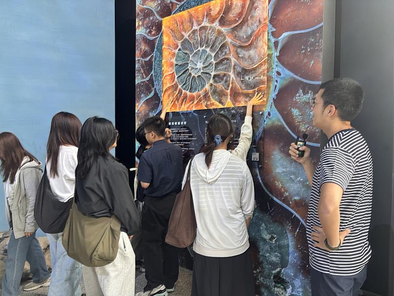 導覽員詹書麟鼓勵學生觸摸鸚鵡螺化石復刻品。
