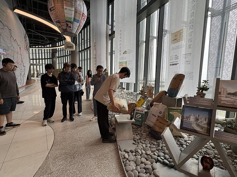 商品展示區扛水泥體驗，後方是各種台泥水泥袋做的熱氣球，左側牆面為台泥全球布局。