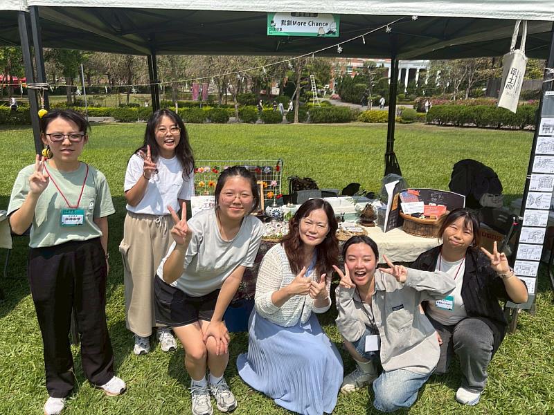 保健系李明明主任(中)帶領學生設置『默釧』師生品牌攤位，與攤位擔任『大頭家』的學生合影。(由左至右: 聽語系楊芮渼、保健系徐可芝、保健系朱于晴、保健系李明明主任、生醫系陸愷焙、資傳系蔡佳誼)