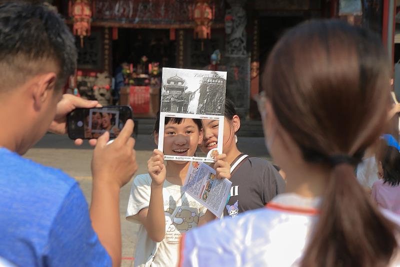 「城西尋跡」活動帶領民眾穿越時空與歷史對話。圖為參與孩童在舊西門遺址所在的西羅殿前，開心地舉起新大西門的歷史老照片打卡合影。