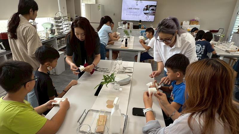 餐飲系師生指導孩童學習餐巾折疊。