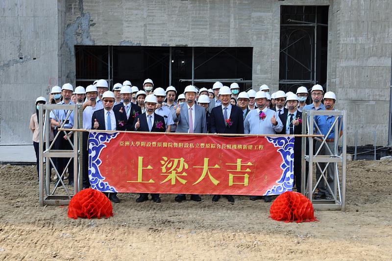 亞大醫療體系團隊與營造夥伴於紅布條前合影，共同見證建設里程碑。