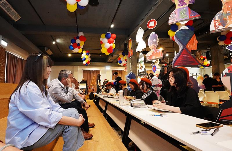 國際設計海報作品以懸吊式裝置呈現，形塑如基因鏈般的視覺流動，結合人物素描戰隊現場創作，使空間氛圍更顯溫潤，也展現跨文化設計的交流對話。