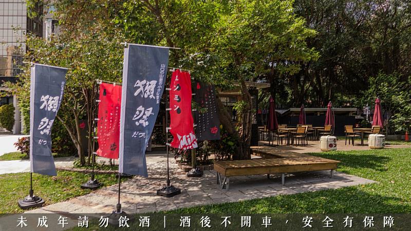 綠意盎然的華山南一館旁，清酒樽與俐落的品牌旗幟交相輝映，營造出宛如置身日本酒造庭園般的愜意微醺氛圍。