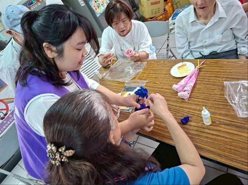 高齡健康照護系（原高齡學程）衛可新校友（左紫背心）引導長輩製作康乃馨吊飾。