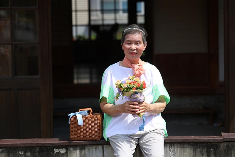 李珠阿嬤拿著花與小籃子等道具，專業擺拍。