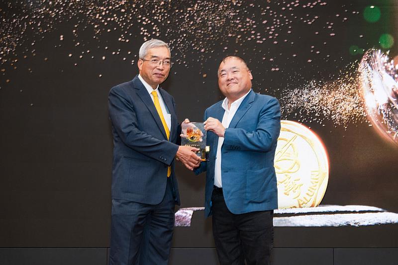 世新大學董事長周成虎（右）致贈紀念琉璃予財信傳媒董事長謝金河（左）。（世新大學提供）