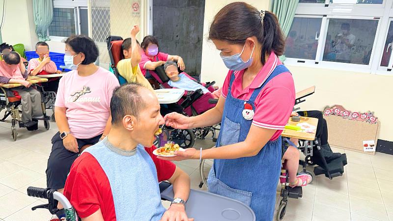 愛維養護中心工作人員細心協助重度身障住民品嚐參賽料理。活動邀請機構服務對象擔任評審進行盲測票選，落實以住民為主體的多元互動與增能成效。