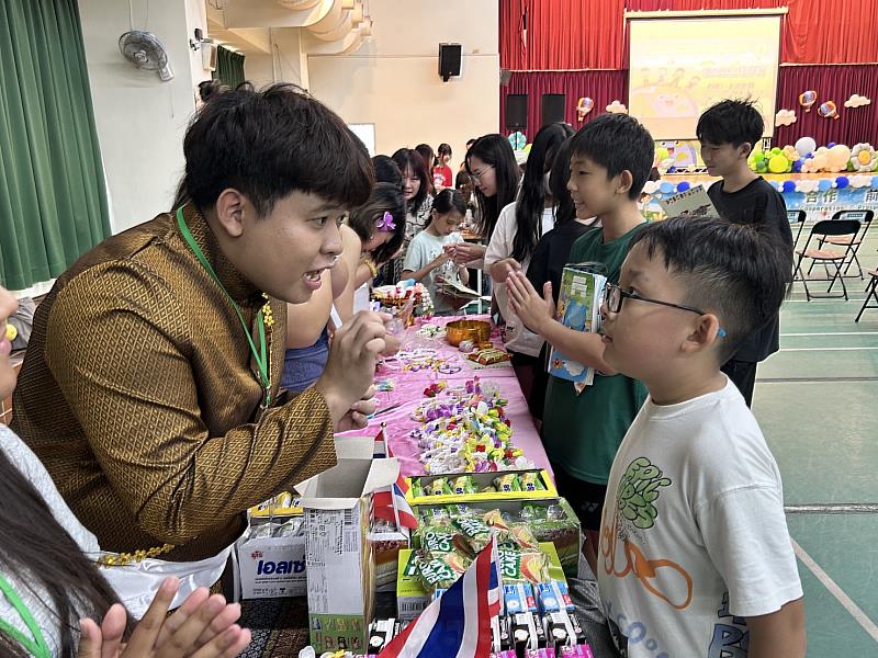 文藻境外生於文化體驗攤位中，身穿泰國傳統服飾向國小學童介紹泰國文化與特色物品，透過互動交流帶領學生認識異國語言、飲食與生活文化。