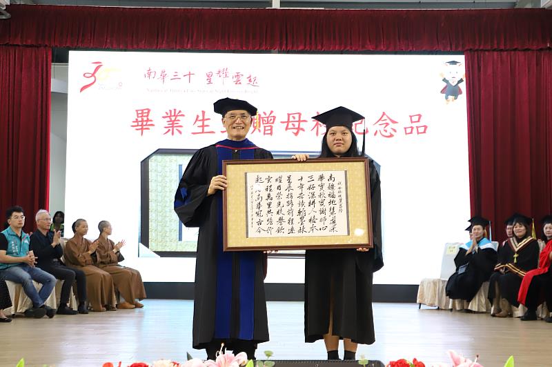 南華大學舉行畢業典禮，畢業生聯合會會長陳思棋(右)代表畢業生致贈以「南華三十、星耀雲起」為題的藏頭詩紀念橫幅予學校，由高俊雄校長(左)代表接受。