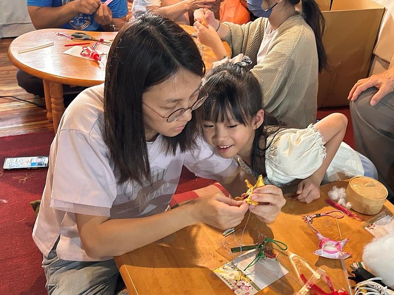 【母女連心・熱縫福加】參與活動的母親溫馨教導女兒如何細心縫製「福加馬」香包，一針一線中展現親子協作的溫暖情景。