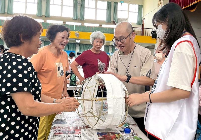 李建盈老闆（右二）親自為傳統鼓仔燈的竹篾骨架進行糊紙示範，社區居民與志工近距離汲取珍貴的古法工藝經驗。