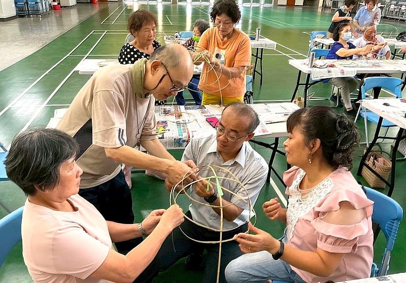 李建盈老闆（左立者）指導鹽水國小林良駿校長（中坐者）與社區居民進行傳統竹製鼓仔燈的骨架編織，手把手傳承瀕危的製作技藝。