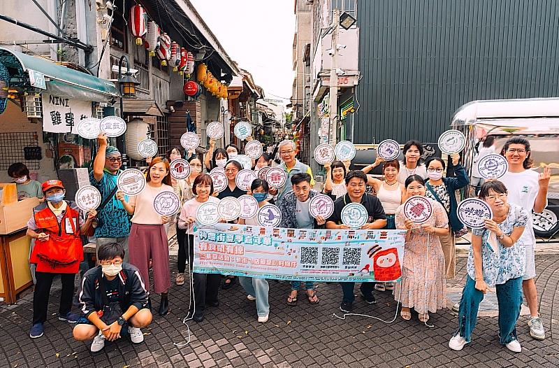 南臺科大USR團隊攜手神農街店家於街口合照,餐與民眾手拿舉牌,為「走入博物館:看老街ㄟ店最夏趴的物件」BINGO集章活動熱情揭幕。