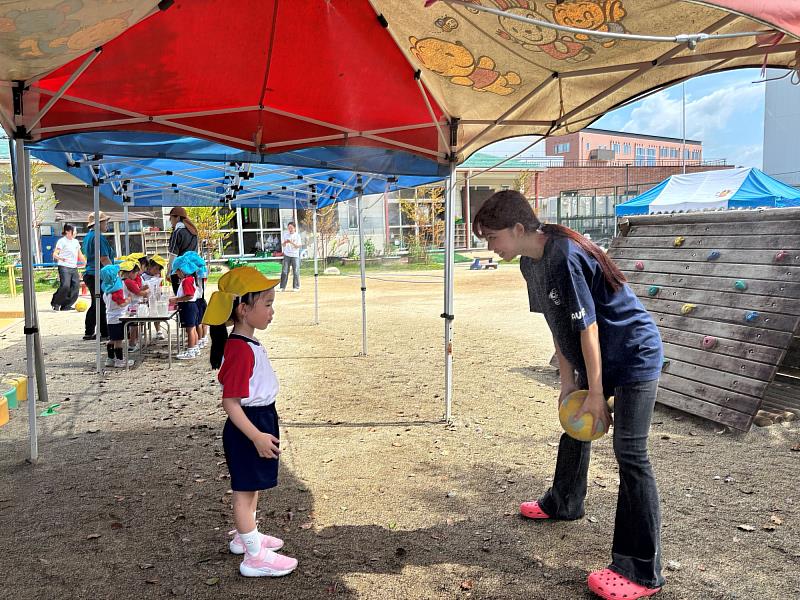 實習生曾詩涵於戶外引導日本幼兒晨間活動,透過互動激發自主學習。