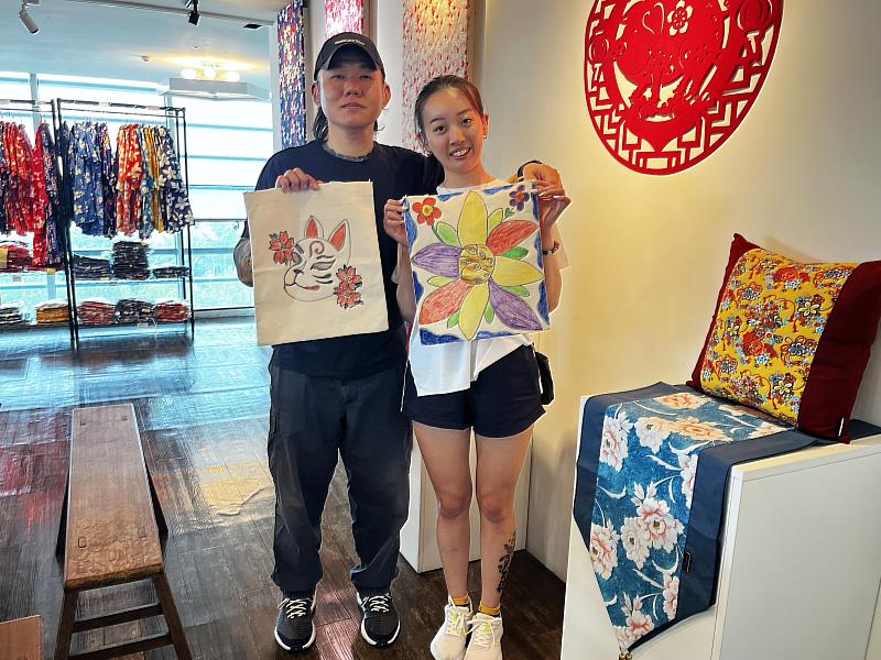 聽障情侶吳善暉(左)與吳翊瑄(右)兩人在手譯員的協助下聆聽說明,嘗試彩繪客家花布提袋,留下屬於兩人的旅遊回憶。