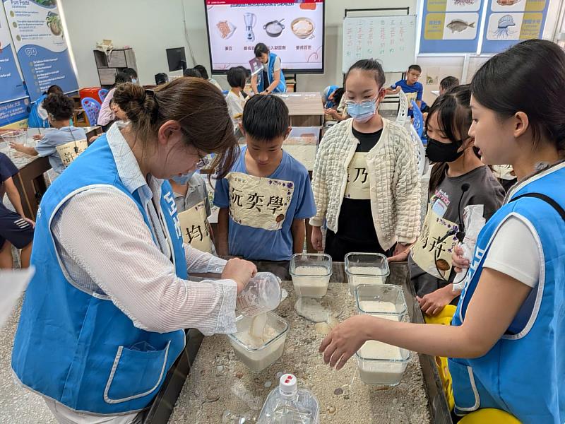 亞大學生張羽榕(右1)為學員講解豆漿凝固原理,並由黃斯榆(左1)示範將熱豆漿沖入凝固劑中,展現寓教於樂的科普實作精神。